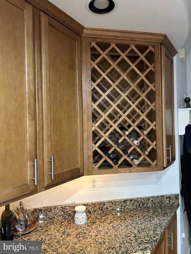 interior details featuring dark stone counters, a bar, and brown cabinets