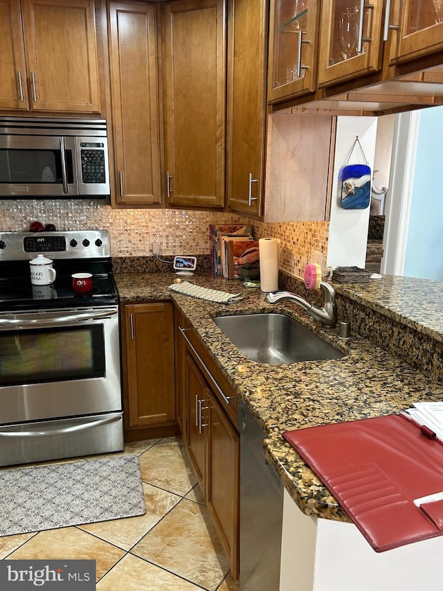 kitchen featuring stainless steel appliances, backsplash, light tile patterned flooring, a sink, and dark stone counters