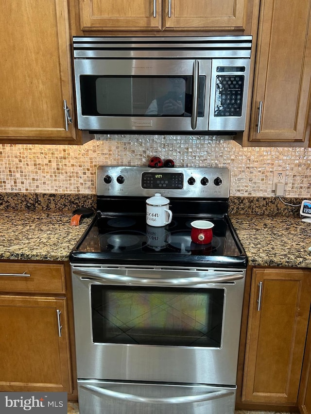 kitchen featuring appliances with stainless steel finishes, dark stone counters, brown cabinets, and tasteful backsplash