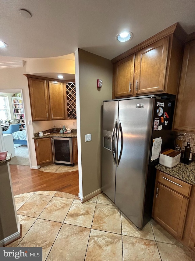 kitchen with beverage cooler, brown cabinetry, dark stone countertops, stainless steel refrigerator with ice dispenser, and light tile patterned flooring