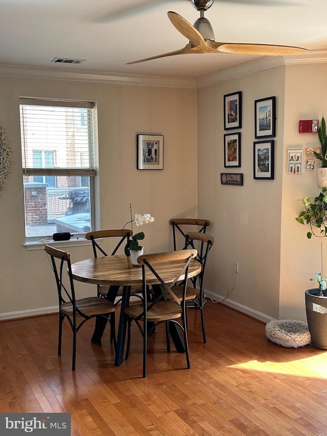 dining area featuring light wood finished floors, baseboards, visible vents, ceiling fan, and crown molding