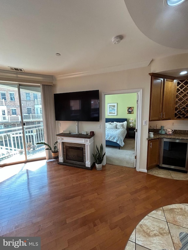 living room featuring wine cooler, a fireplace, visible vents, ornamental molding, and light wood finished floors