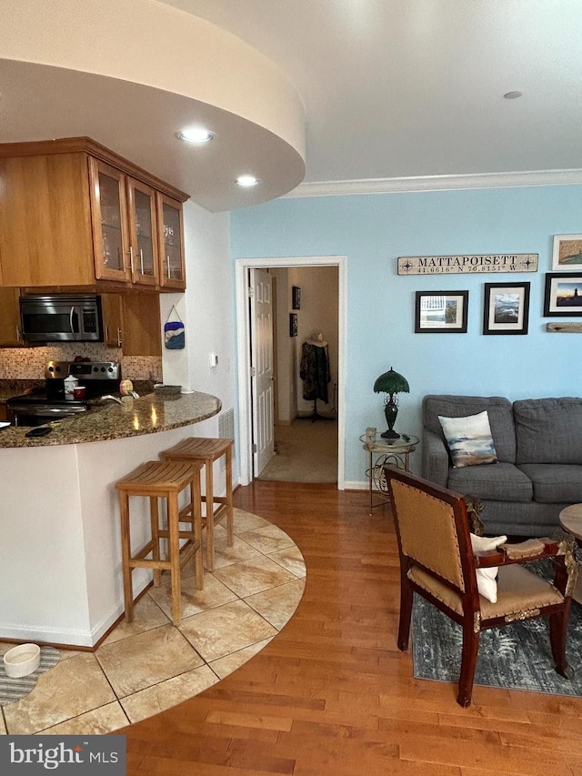 kitchen with brown cabinetry, glass insert cabinets, appliances with stainless steel finishes, crown molding, and light wood-style floors