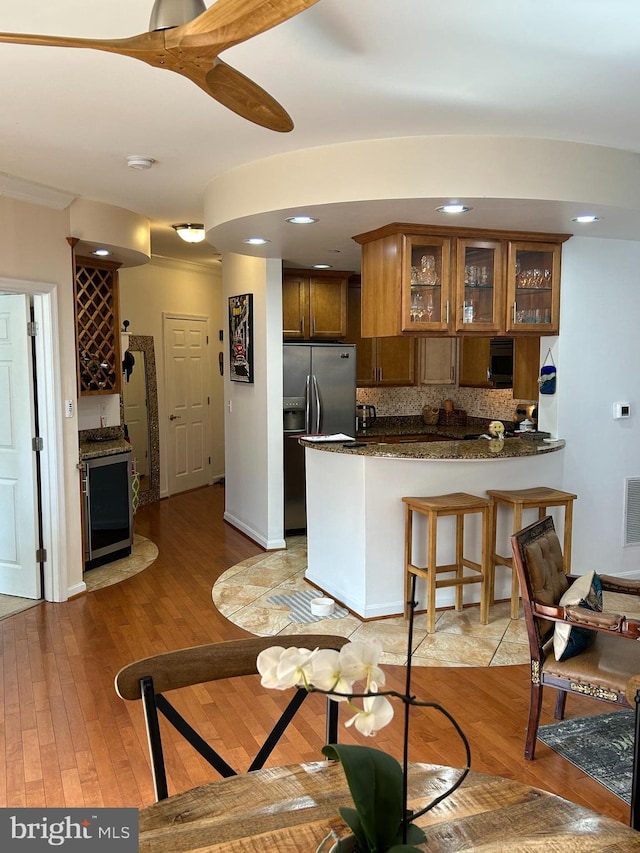 kitchen featuring brown cabinets, stainless steel refrigerator with ice dispenser, tasteful backsplash, light wood-type flooring, and a peninsula