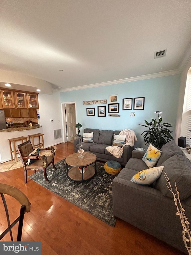 living area with crown molding, visible vents, and wood finished floors