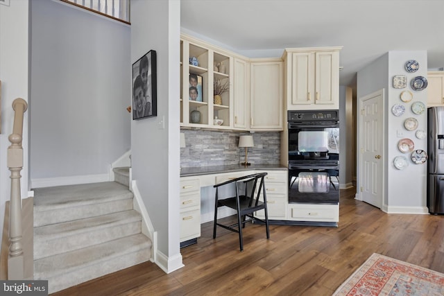 kitchen featuring cream cabinets, dobule oven black, dark wood-type flooring, stainless steel refrigerator with ice dispenser, and decorative backsplash