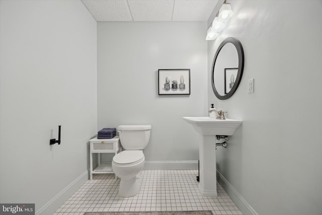 half bathroom with toilet, baseboards, a drop ceiling, and tile patterned floors