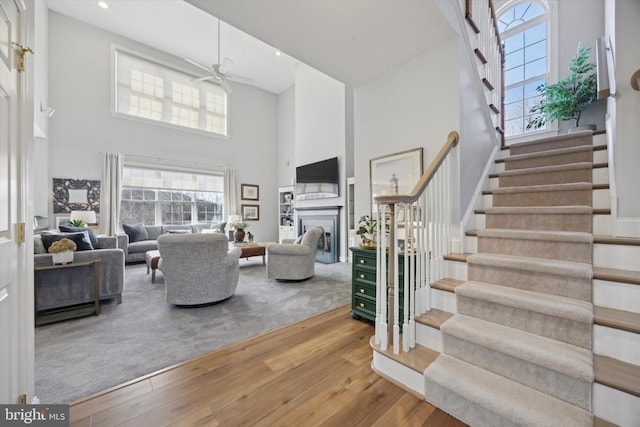 living area with stairs, hardwood / wood-style floors, a fireplace, and a towering ceiling