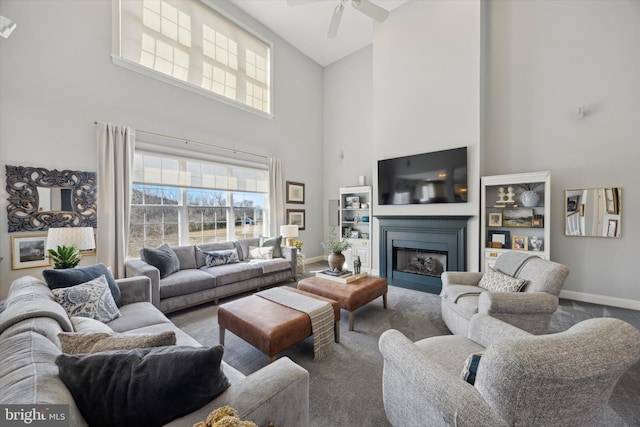 living area featuring baseboards, a towering ceiling, ceiling fan, carpet, and a fireplace