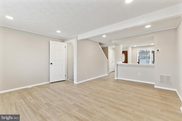 unfurnished living room featuring light wood finished floors, visible vents, a textured ceiling, and baseboards