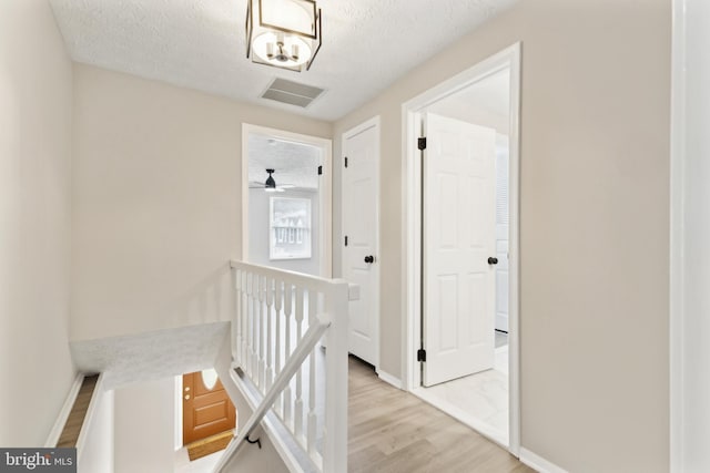 corridor with wood finished floors, baseboards, visible vents, a textured ceiling, and an upstairs landing