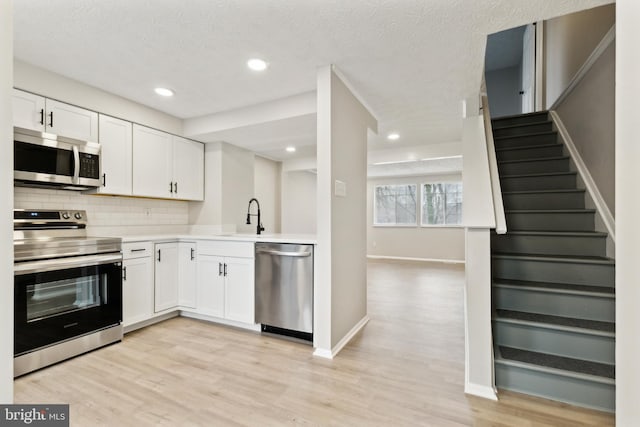 kitchen featuring a sink, backsplash, appliances with stainless steel finishes, white cabinets, and light countertops