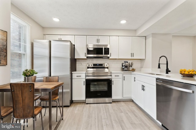 kitchen with light wood finished floors, appliances with stainless steel finishes, light countertops, and a sink