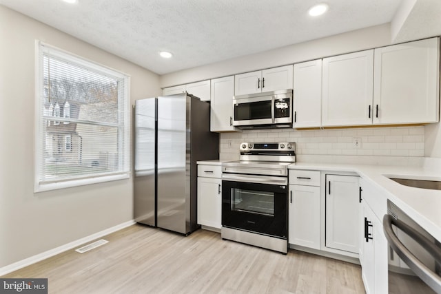 kitchen featuring light wood finished floors, visible vents, light countertops, decorative backsplash, and appliances with stainless steel finishes