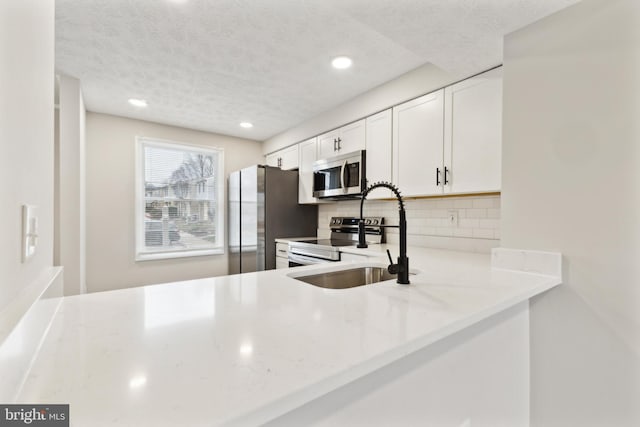 kitchen featuring a peninsula, a sink, stainless steel appliances, white cabinetry, and backsplash