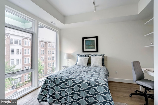 bedroom featuring a raised ceiling, rail lighting, visible vents, wood finished floors, and baseboards