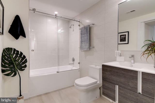 full bathroom featuring visible vents, bath / shower combo with glass door, toilet, vanity, and tile walls