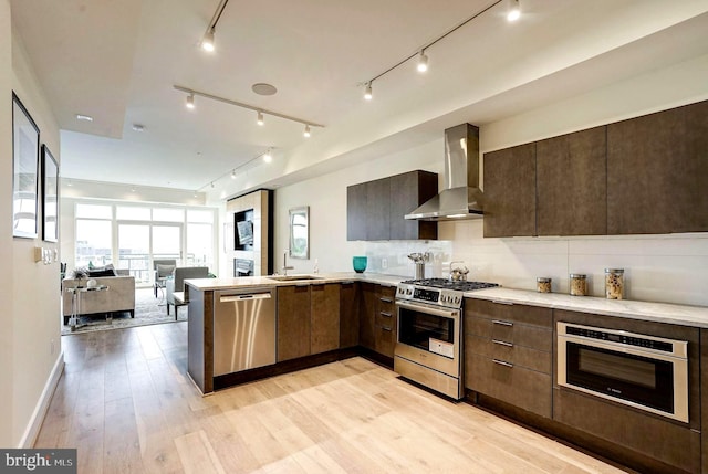 kitchen featuring stainless steel appliances, open floor plan, wall chimney exhaust hood, light wood finished floors, and modern cabinets