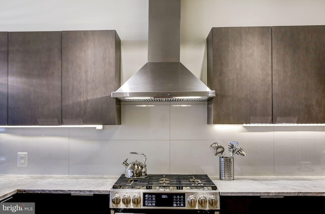 kitchen with decorative backsplash, dark brown cabinetry, wall chimney range hood, modern cabinets, and stainless steel gas range oven