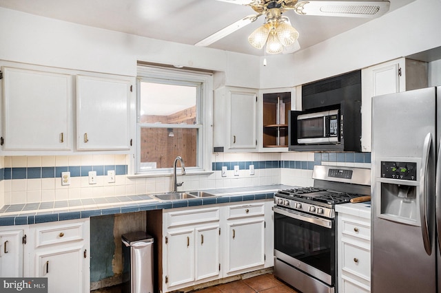 kitchen featuring a sink, backsplash, white cabinetry, tile countertops, and appliances with stainless steel finishes