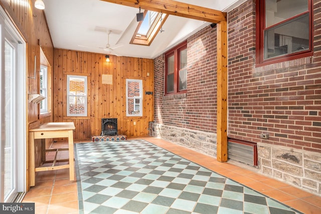 unfurnished sunroom featuring vaulted ceiling with skylight and a wood stove