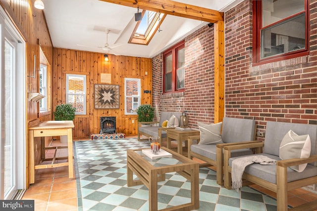 interior space featuring lofted ceiling with skylight, wooden walls, a ceiling fan, and brick wall