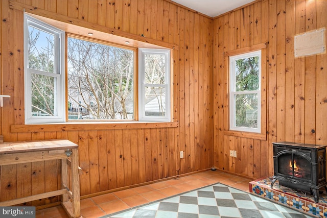 unfurnished room featuring tile patterned floors, a wood stove, baseboards, and wood walls