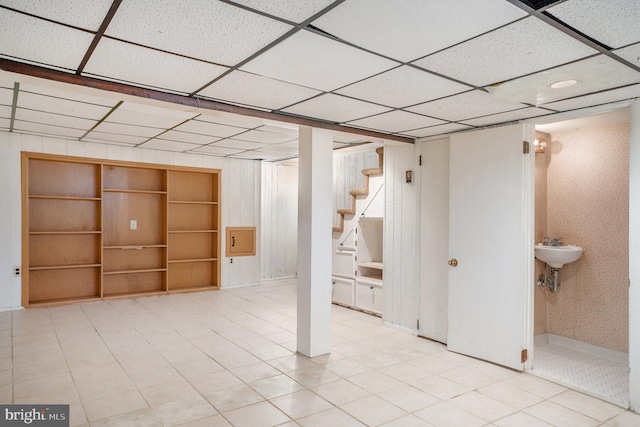 finished basement with stairway, a paneled ceiling, and a sink