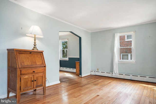 empty room featuring light wood finished floors, a baseboard heating unit, and ornamental molding