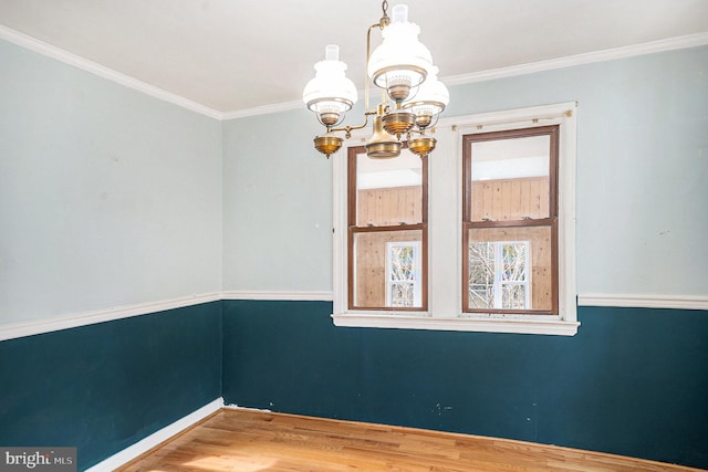 empty room featuring an inviting chandelier, wood finished floors, baseboards, and ornamental molding