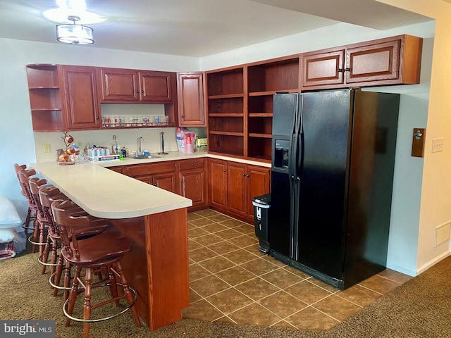 kitchen featuring a peninsula, a sink, black fridge, open shelves, and a kitchen bar