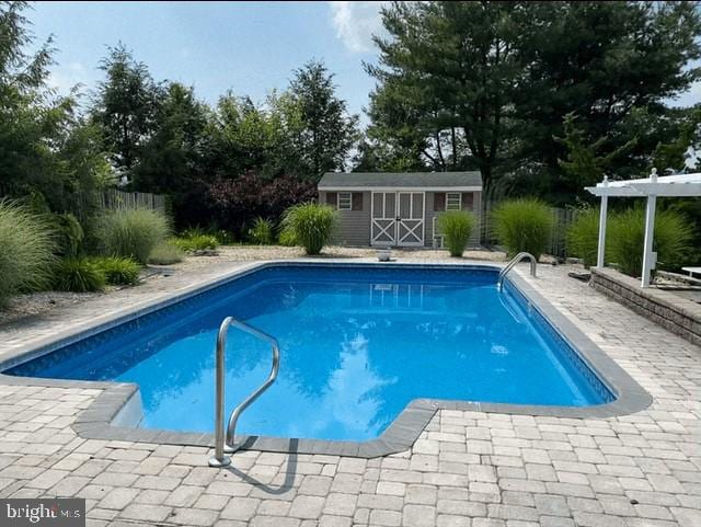 outdoor pool featuring a patio area, a shed, a pergola, and an outbuilding