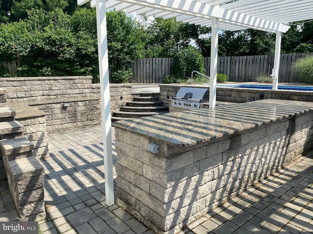 view of patio with exterior kitchen, a fenced backyard, grilling area, and a pergola