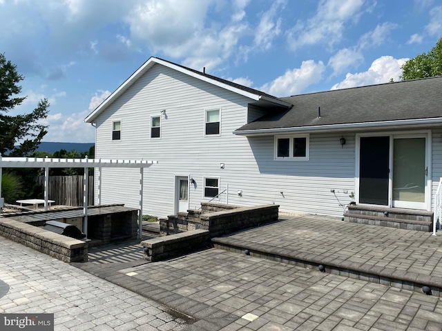 back of property with entry steps, a hot tub, a patio, exterior kitchen, and a pergola