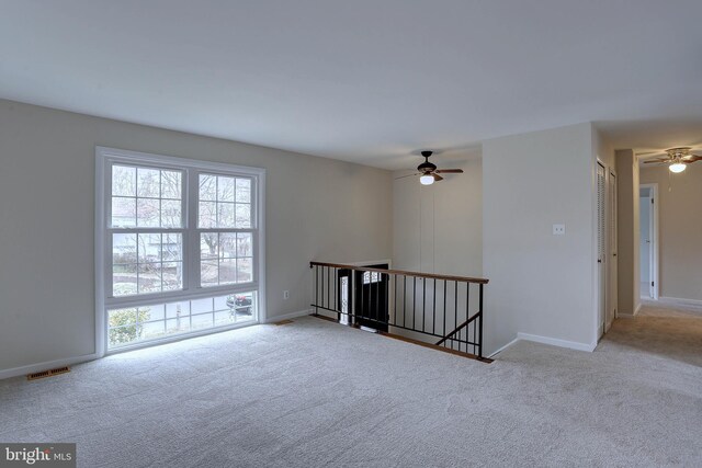 carpeted spare room with a ceiling fan, visible vents, and baseboards