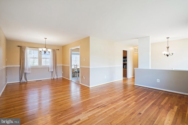 empty room with visible vents, baseboards, light wood-style floors, and an inviting chandelier