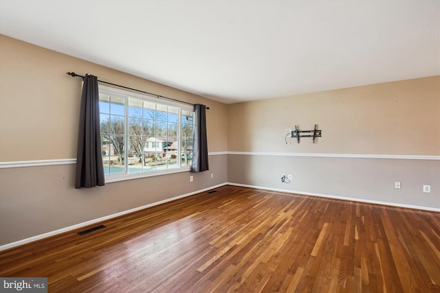 unfurnished room with wood finished floors, visible vents, and baseboards