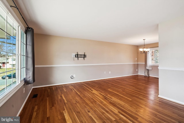 unfurnished room with a notable chandelier, visible vents, baseboards, and wood finished floors