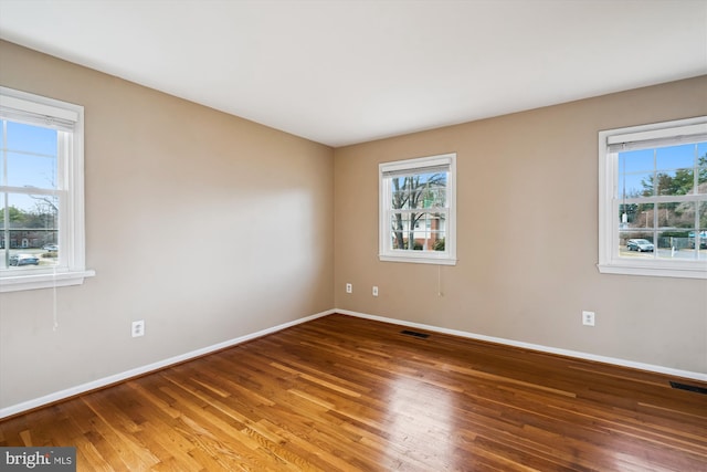 unfurnished room featuring visible vents, a healthy amount of sunlight, and wood finished floors