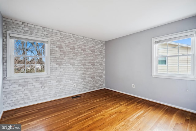 unfurnished room featuring visible vents, baseboards, wood finished floors, and brick wall