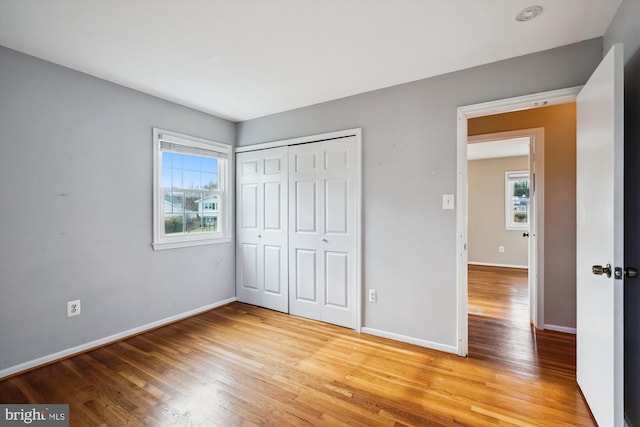 unfurnished bedroom with a closet, multiple windows, baseboards, and light wood finished floors