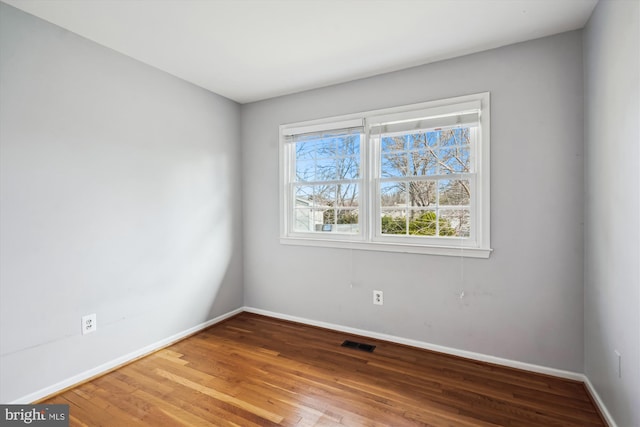 spare room featuring wood finished floors, visible vents, and baseboards