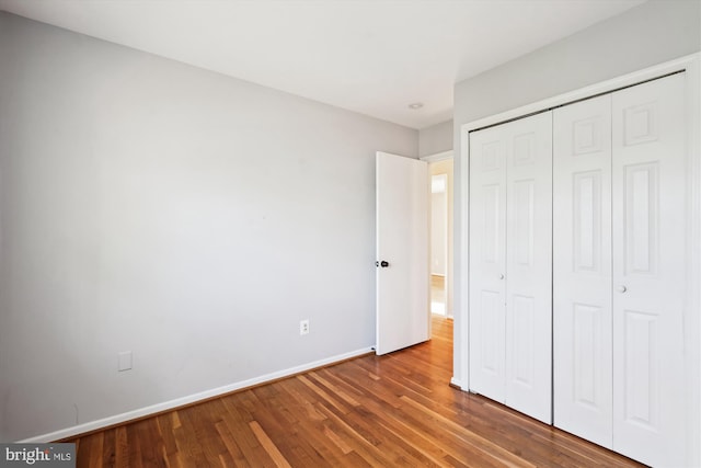 unfurnished bedroom featuring wood finished floors, baseboards, and a closet