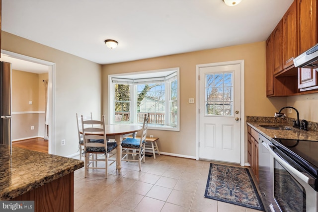 kitchen with brown cabinets, a sink, appliances with stainless steel finishes, light tile patterned flooring, and baseboards