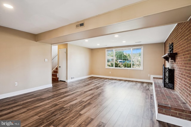 unfurnished living room featuring dark wood finished floors, a brick fireplace, stairs, and visible vents