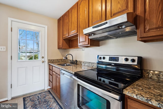 kitchen with under cabinet range hood, appliances with stainless steel finishes, brown cabinetry, and a sink