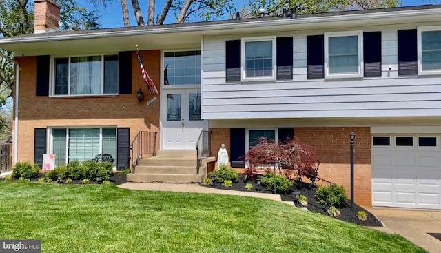 split foyer home with french doors, a front yard, an attached garage, brick siding, and a chimney