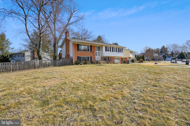 bi-level home featuring brick siding, a chimney, a front yard, and fence