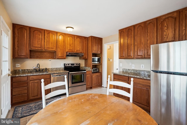 kitchen featuring under cabinet range hood, appliances with stainless steel finishes, and brown cabinetry