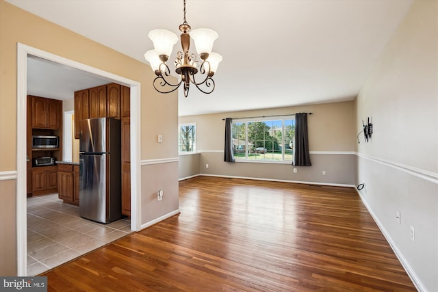 unfurnished dining area with a notable chandelier, baseboards, and wood finished floors